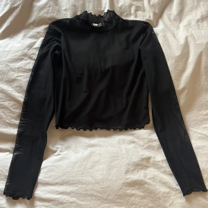 Svart mesh polotopp från Pull&Bear - Säljer en svart mesh polotopp från Pull&Bear i storlek S. Toppen har lång ärm, croppad passform och en hög krage med volangkant. Sparsamt använd och helt utan hål.