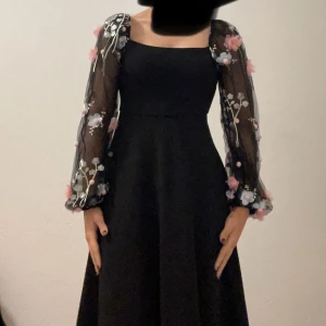 Svart långklänning med blommiga ärmar - Svart långklänning med fyrkantig urringning och transparenta långärmar dekorerade med broderade blommor i rosa och blått.  Är runt 165-168 cm 💕| pris kan diskuteras |