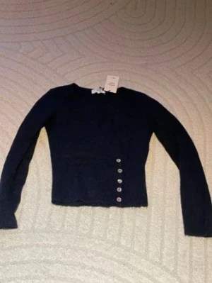 Mörkblå stickad tröja med knappar - Snygg mörkblå stickad tröja från Gina Tricot med lång ärm och dekorativa knappar på sidan av midjan. Tröjan har en rund halsringning och är figurnära i modellen, perfekt för att lyfta din outfit med en cool detalj. Nypris 459 helt ny lappen sitter kvar!