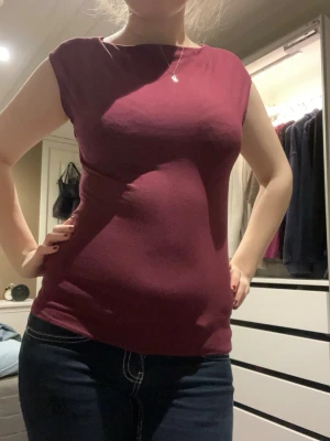 Vinröd ärmlös topp i bomull - Säljer en vinröd topp med ärmlös design och rund hals. Toppen är figurnära och har en enkel, stilren look utan mönster eller detaljer. Materialet känns mjukt och stretchigt, troligen bomull. Perfekt att matcha med jeans eller kjol.