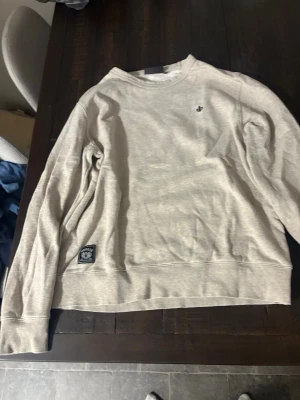 Beige sweatshirt från Morris, M - Snygg beige sweatshirt från Morris med rund hals och ribbade muddar. Tröjan har ett diskret Morris-emblem på bröstet och en patch vid bröstet 