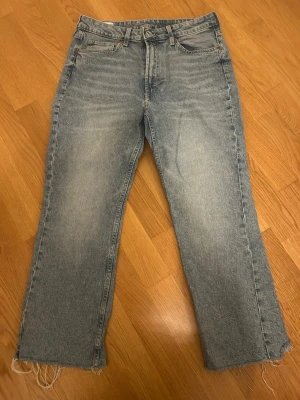 Blå croppade flare jeans - Säljer ett par blå jeans från &Denim och croppad flare-modell. Jeansen har klassisk femficksdesign, råa kanter vid benslut och är tillverkade i denim. Perfekt för dig som gillar en chill och trendig look.