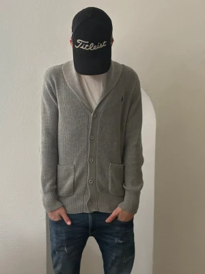 Exklusiv cardigan från Polo Ralph Lauren - Säljer en grå ribbstickad kofta från Polo Ralph Lauren i storlek M. Koftan har knappar framtill, två fickor och en klassisk sjalkrage. Diskret logga broderad på bröstet. Perfekt för lager på lager under höst och vinter. Jag köpte den på en mall i london för 199€ som är ca 2300 kr modellen är 184 så om du är 182-190 är den perfekt skulle jag säga hör av dig vid funderingar 