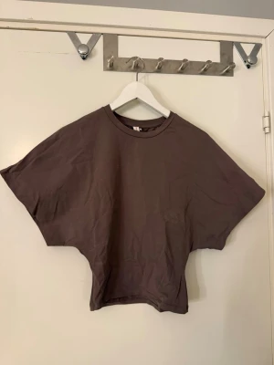 Brun t-shirt från Nelly - Säljer en brun t-shirt från Nelly i storlek S. Modellen är tajt i midjan med lösa armar och rund halsringning. Materialet är mjuk bomull och färgen är mörkbrun. Perfekt för en chill och avslappnad stil.