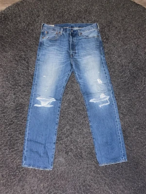 Levi's 501 blå jeans med slitningar - Säljer ett par Levi's 501 jeans eftersom dom ej kommit till någon användning Storlek W34 L32, rak passform. Pris går att diskuteras 