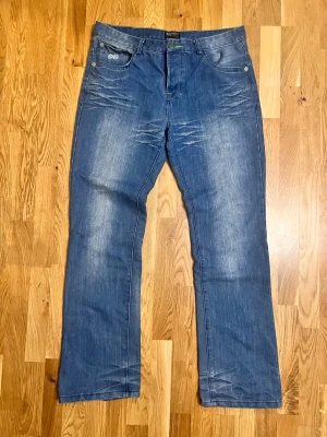 Blå bootcut jeans från Stanwick, storlek 36/32 - Snygga blå jeans från Stanwick med coola kontrastsömmar i gult och brunt. Klassisk femficksmodell med unika detaljer på bakfickan och knappstängning. Jeansen har rak passform och är tillverkade i slitstarkt denimtyg. Perfekt för dig som gillar streetstyle.