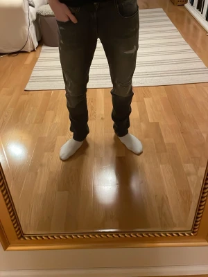 Replay svarta slitna jeans - Säljer ett par svarta Replay jeans med slitningar och distressed detaljer på benen. Jeansen har en smal passform och klassisk femficksdesign. Snyggt tvättade med gråtoner och coola slitna partier för en trendig look.