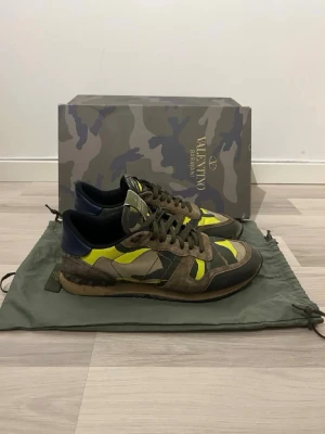 Valentino Rockrunner sneakers camouflage - Säljer ett par Valentino Rockrunner sneakers med grymt camouflage-mönster i brunt, grönt, gult och mörkblått. Skorna har snörning, platt sula och detaljer i mocka och skinn. Perfekt för dig som vill sticka ut med en fet design och coola färgkombinationer.