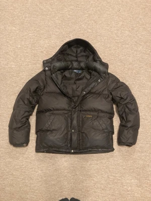 Svart pufferjacka från Polo Ralph Lauren - Polo Ralph Lauren vinterjacka i gott skick!  Jackan har använts så är lite sliten på vissa ställen men inget som påverkar funktion, den är lite blekt vid halsen troligen av smink, men det syns inte utifrån, kort och gott en jacka i bra skick av ett fint märke. Personen på bilden är 180 cm