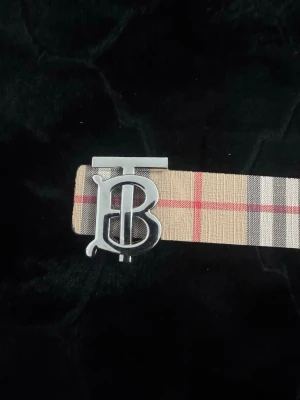  Burberry bälte - Säljer en snygg väst från Burberry med klassiskt rutigt mönster i beige, rött, svart och grått. Västen har en stilren form och är tillverkad i ett slitstarkt material med en lyxig känsla. Perfekt för dig som vill ha en ikonisk och trendig look.