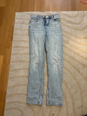 Ljusblå straight jeans från H&M  - Säljer ett par ljusblå straight fit jeans från &Denim i storlek 34. Modellen har hög midja, klassiska fem fickor och bälteshällor. Jeansen är tillverkade i bomull och har en snygg tvättad look med dragkedja och knapp framtill.
