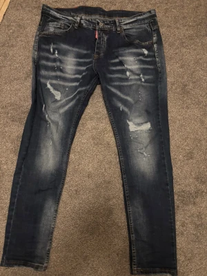 Dsquared2 skinny jeans med röd patch - Snygga mörkblå jeans från Dsquared2 med slitningar och tvättade detaljer framtill. Baktill finns en röd patch med grafiskt tryck och text. Jeansen har klassisk femficksdesign och smal passform som sitter tajt längs benen.