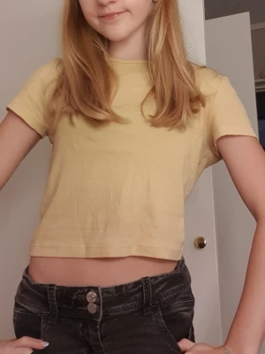 Gul ribbad t-shirt från H&M Divided - Säljer en ljusgul ribbad t-shirt från H&M Divided i storlek S. T-shirten har korta ärmar och är croppad i modellen, vilket gör den perfekt till jeans eller shorts. Materialet är mjukt och skönt bomull. Enkel och gullig stil.