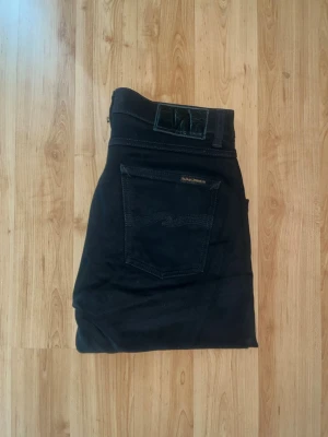 Nudie Jeans - Svarta jeans från Nudie Jeans. Midja 38cm, längd 99cm. OBS jeansen har diskreta defekter på låren - se bild på de omringade områdena. JAG SKICKAR EJ FLER BILDER NÄR JAG BÄR JEANSEN! för bättre inblick i passformen rekommenderar jag att googla på modellnamnet. För storleksguide kolla måtten noggrant då jeansen alltid kan vara uppsydda heller krympta och jag ej tar emot returer :) s5,2