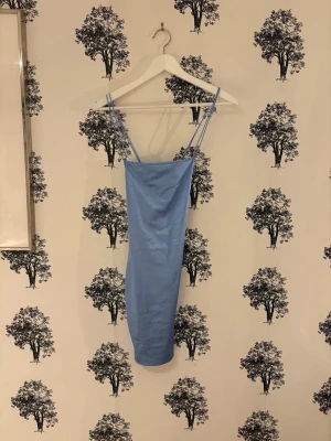 Blå satin klänning från H&M - Säljer en ljusblå kortklänning från H&M i glansigt satinmaterial. Klänningen har smala axelband och en figurnära passform som ger en snygg siluett. Perfekt för dig som gillar stilrena och trendiga plagg med lite extra shine.