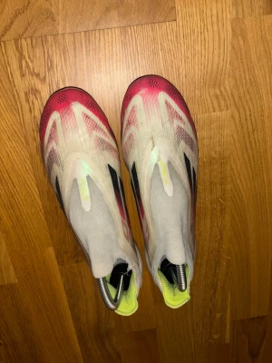 Adidas F50 fotbollsskor vit/röd - Säljer ett par Adidas F50 fotbollsskor med en snygg vit bas och röda samt svarta detaljer. Skorna har en strömlinjeformad design, platt sula med dobbar och inslag av gult på insidan och undersidan. Tillverkade i syntetmaterial för lätt känsla på planen.