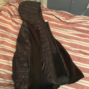 Svart pufferjacka från McKinley - Svart pufferjacka från McKinley i storlek small. Jackan har huva, dragkedja och quiltad design med horisontella sömmar. Materialet är syntet och polyester, vilket gör den lätt och skön att bära. Perfekt för kyliga dagar och enkel att matcha med din stil. kan ändra pris beror på