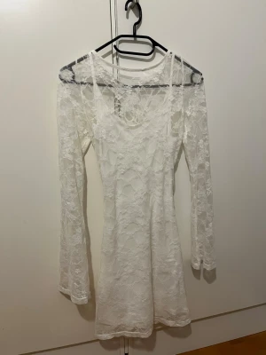 Studentklänning i spets vit  - Supersöt vit kortklänning från H&M i storlek XS. Klänningen har långa ärmar, är gjord i spets och har snygg snörning i ryggen. Använd endast en gång. 