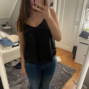 Svart linnetopp från Lager 157 - Säljer en stilren svart linnetopp från The Black Label Collection. Toppen har en enkel design med tunna axelband och en lös passform. Lite öppen i ryggen. Perfekt för en minimalistisk look. Hör av dig vid intresse!