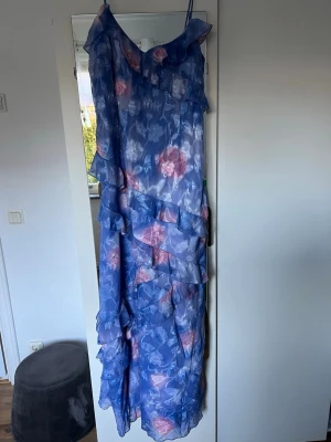 Blommig blå långklänning Boohoo - Säljer en blå långklänning från Boohoo med tunna axelband och volangdetaljer. Klänningen har ett blommigt mönster i rosa och vitt.