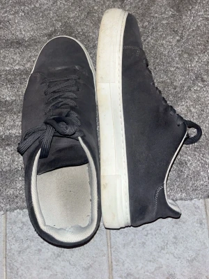 Mörkgråa sneakers med vita sula - Säljer ett par mörkgråa sneakers från Selected Homme i storlek 44 som jag köpte för 1100 kr. Skorna har en stilren design med vit platt sula, rund tå och snörning. Utsidan är i mocka och insidan är fodrad med ljusgrå textil. Perfekta för dig som gillar enkel och klassisk stil, som ni kan se är det lite sönder vid hälen på skorna men det är inget man märker av vid användning o det är därför jag säljer dessa till så billigt pris!👍Tveka inte på att ställa en fråga eller två det skader inte☺️☺️🙏