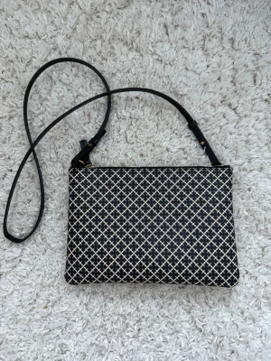 By Malene Birger - Snygg axelväska från By Malene Birger med svart och vit rutigt mönster. Väskan har en smal axelrem i svart och guldfärgad dragkedja. Insidan är fodrad i en brunrosa ton. Perfekt storlek för det viktigaste och stilren design. Bredd 25,5cm och höjd 18cm