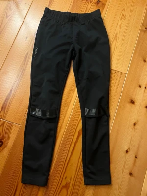 Craft Juniors' Adv Warm Xc Tights Black - Säljer ett par svarta längdskidbyxor från Craft i juniorstorlek 146/152. Byxorna har elastisk midja och snygga detaljer med blanka paneler vid benen. 