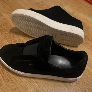 Svarta sneakers från Axel Arigato - Stilrena svarta sneakers från Axel Arigato i mocka i storlek 43. Köpta under sommaren och väldigt väl använda 8/10 skick. Perfekta för dig som gillar design och modern stil. Defekter skulle jag säga är några småfläckar på mockan. Fler bilder dm.