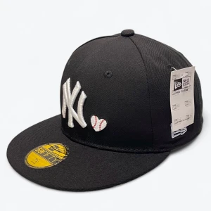 Svart New Era Yankees keps 59FIFTY 7 1/8 56.8 cm  - Svart New Era 59FIFTY keps med broderad vit NY Yankees-logga och ett litet hjärta som ser ut som en baseboll. På sidan finns en färgglad World Series 1996-patch. Klassisk rak skärm och snygg streetstil, perfekt för dig som gillar sport och snygga accessoarer.