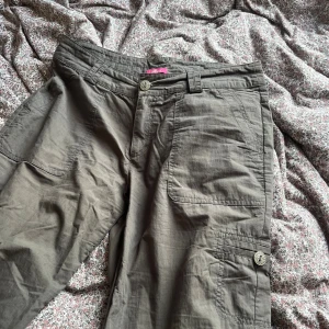 Khakigröna cargopants från Hillevi - Snygga khakigröna cargopants från Hillevi med stora fickor på sidorna och bak. Byxorna har raka ben, bälteshällor och coola detaljer som knappar med mönster. Perfekta för en avslappnad och trendig stil.