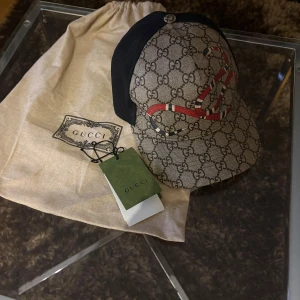 Gucci keps med GG-mönster och orm - Snygg keps från Gucci med klassiskt GG-monogram i beige och brunt, prydd med en röd och svart orm framtill. Insidan är i svart mesh för extra ventilation. Kepsen kommer med originalpåse och taggar kvar.