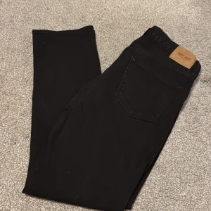 Svarta jeans Baxter från East West - Svarta jeans från East West, modell Baxter Regular Fit. Klassisk femficksdesign med svart tonad sömnad och läderpatch bak i midjan. Jeansen är raka i modellen och tillverkade i bomull med lite stretch för extra komfort.