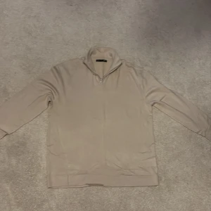 Beige halvzip tröja i bomull - Snygg beige långärmad tröja med half zip och hög krage. Perfekt för dig som gillar en clean och stilren look. Tillverkad i mjuk bomull som känns skön mot huden. Passar till både jeans och mjukisbyxor.