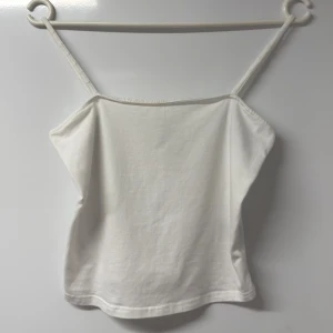 Vit linnetopp från H&M Divided - Säljer en enkel och fräsch vit linnetopp från H&M Divided i storlek S. Toppen har smala axelband och är tillverkad i mjuk bomull med lite stretch för skön passform. Perfekt att styla med jeans eller kjol för en clean look.
