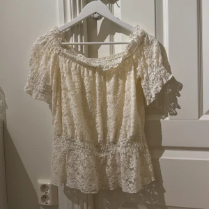 Offshoulder spetsblus från Bodyflirt - Offshoulder blus i cremevitt från Bodyflirt. Blusen är täckt av vacker spets, har korta ärmar och volangkant nertill. 💞