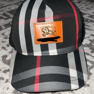 Svart keps  - Snygg keps med klassiskt rutigt mönster i svart, grått, vitt och rött. . Baksidan är i svart mesh för extra ventilation. Perfekt för dig som vill ha en statement-accessoar.