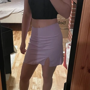 Ljuslila kortkjol med slits - Snygg ljuslila kortkjol med en liten slits framtill. Kjolen har en enkel och stilren design med rak passform och hög midja. Perfekt för dig som gillar minimalistisk stil och vill ha något som sticker ut med färgen. Materialet känns mjukt och lätt mot huden.