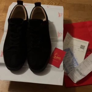 Christian Louboutin skor - Svarta sneakers från Christian Louboutin med ikonisk röd sula och snygg signatur på undersidan. Skorna har rund tå, platt sula och är tillverkade i mjuk mocka med svarta snören. Perfekt för dig som vill ha en lyxig och stilren look. Storlek 44 passar även 43, kan liven gå ner i pris vid snabb affär