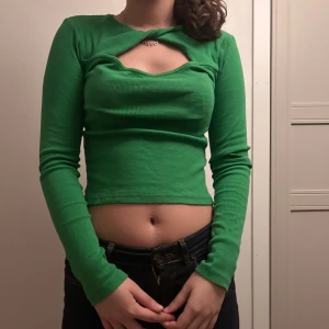 Grön croppad långärmad topp Gina Tricot - Snygg grön långärmad topp från Gina Tricot med croppad passform och cool twistad detalj vid halsen som skapar en öppen rygg och cut-out framtill. Ribbad struktur i stretchigt material🥰🥰.