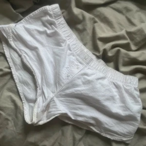 Vita låg midjade shorts med rosett - Säljer ett par söta vita lågmidjade shorts i bomull med diskret rutigt mönster. De har knappar framtill, spetskant och en liten rosett i sidan☺️