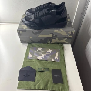 Valentino Garavani Rockrunner sneakers - Snygga Valentino’s Garavani Rockrunner sneakers i svart med grått kamouflagemönster. Skorna har en mix av skinn, mocka och textil, samt coola nitar på sulan. Klassisk snörning och rund tå. Kommer med originalkartong och dustbag.