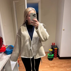 Beige omlottjacka från Vila - Säljer en beige omlottjacka från Vila i storlek 36. Jackan har knytband i midjan, dekorativa kanter och en loose passform. Perfekt för lager-på-lager och har en stilren, enkel look med lång ärm. 599 ny, använd en gång