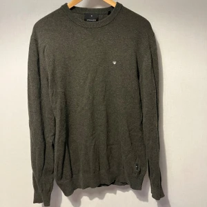 Stickad tröja  - Ny snygg mörkgrå stickad tröja från Junk de Luxe med rund hals och diskret logga på bröstet. Tillverkad i en mjuk blandning av återvunnen italiensk lammull. Perfekt för dig som gillar stilrena och enkla plagg med en chill vibe. Nypris 899kr.