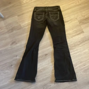 Svarta bootcut jeans från Gina Tricot - Svarta jeans från Gina Tricot med tydliga vita kontrastsömmar och bootcut-ben. Klassisk femficksmodell med snygga detaljer på bakfickorna och knapp med logga framtill. Jeansen har låg midja och är tillverkade i ett jeansmaterial.