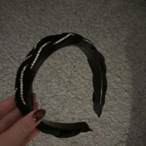 Svart diadem med pärldetaljer - Snyggt svart diadem i sammet med flätad design och glittrande pärldetaljer i vågigt mönster. Perfekt accessoar för att lyfta din look med lite extra bling och stil.