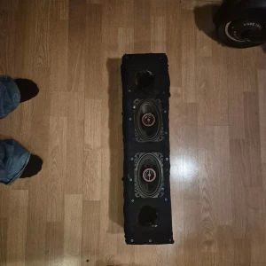 Raggar planka  - Snygg högtalarlåda med två inbyggda bilhögtalare, perfekt för ljuduppgradering i bilen. Svart tygklädd låda med synliga monteringsskruvar. Viss slitage och två tomma hål upptill och nedtill, men högtalarna ser hela ut. Säljs i befintligt skick. 250w rms styck cerwin vega passar i hatthylla