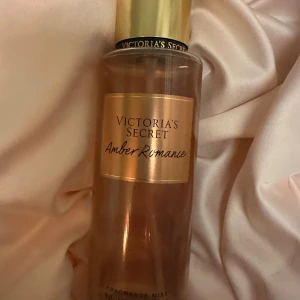 Amber Romance Fragrance Mist - Victoria's Secret - Säljer en Amber Romance Fragrance Mist från Victoria's Secret. Flaskan är genomskinlig med en gyllene etikett och lock. Doften har toner av djup amber och sockerkyssar, perfekt för att fånga solnedgångens magi.