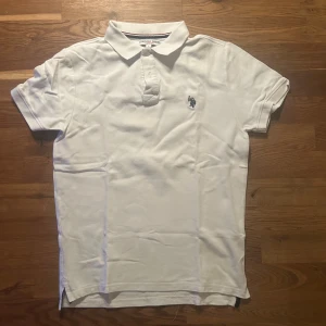 Vit pikétröja från U.S. Polo Assn. - Vit pikétröja från U.S. Polo Assn. i klassisk design med krage och kort knappslå. Tröjan har ett broderat mörkblått polospelar-märke på bröstet och är tillverkad i mjuk bomull. Passar dig som gillar stilrena och sportiga plagg. Nypris 1250kr köpt inför denna sommaren! Pris går att diskutera vid snabb affär.