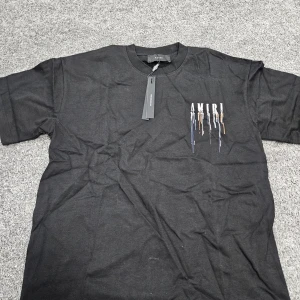 Svart AMIRI t-shirt med färgstänk - Svart t-shirt från AMIRI med coolt tryck av droppande färg och stor logga både fram och bak. T-shirten har rund hals, korta ärmar och är gjord i mjuk bomull. Perfekt för dig som vill sticka ut med streetstyle-vibe.