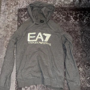 Grå EA7 Emporio Armani hoodie - Säljer en grå hoodie från EA7 Emporio Armani med stor logga framtill.